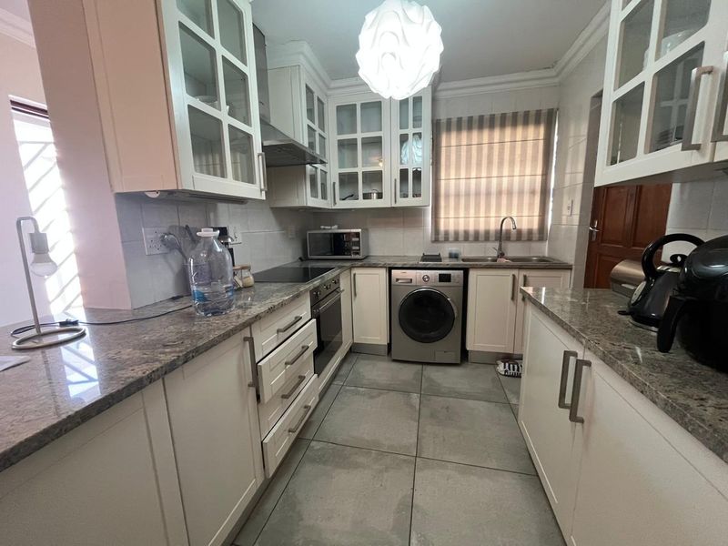 A functional kitchen featuring granite countertops, glass-fronted cabinetry, built-in oven, electric hob, and an integrated washing machine.