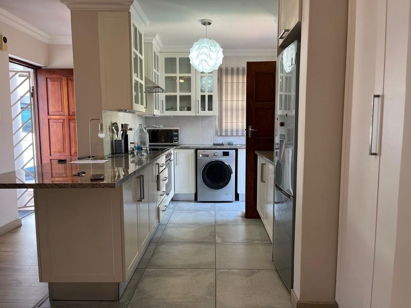 A well-maintained kitchen featuring granite countertops, ample built-in cabinetry with glass-fronted uppers, integrated appliances, and neutral tiled flooring.