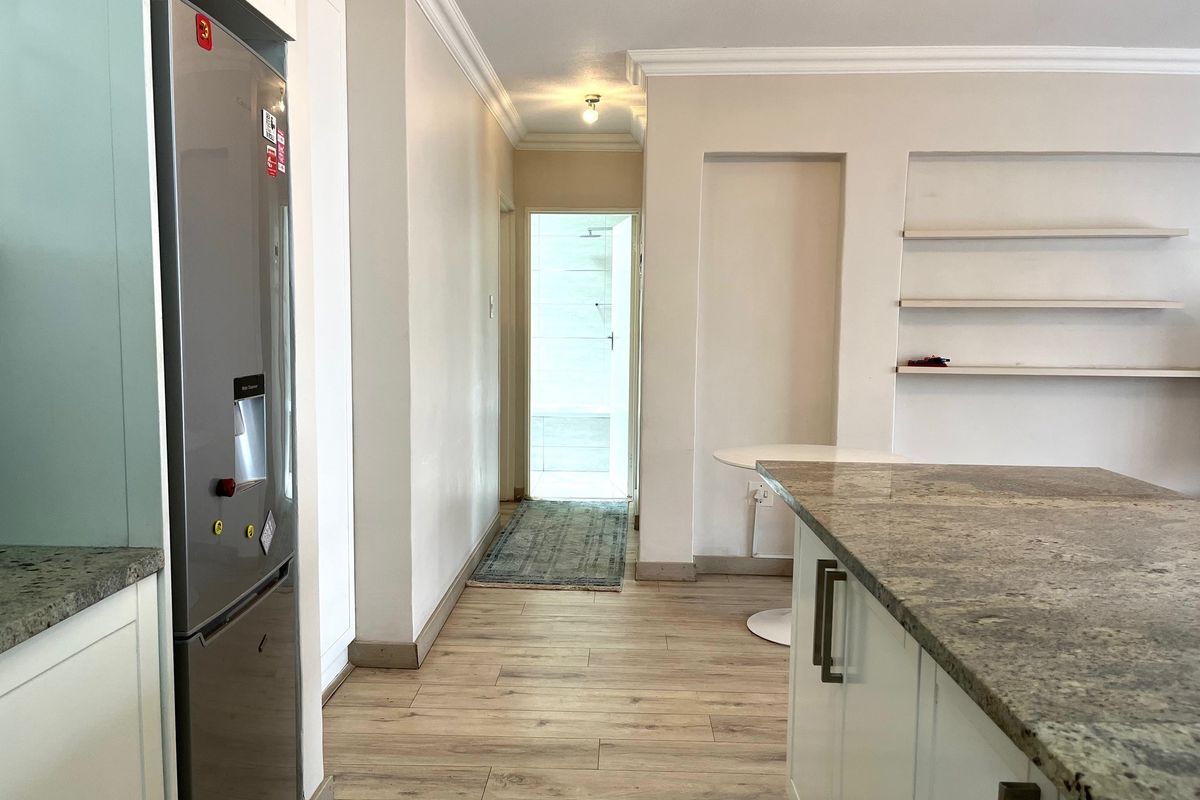 A modern kitchen area featuring granite countertops, built-in cabinetry, and laminate flooring, leading into a hallway with recessed shelving.