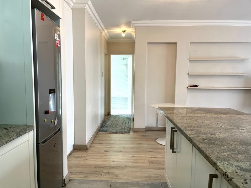 A modern kitchen area featuring granite countertops, built-in cabinetry, and laminate flooring, leading into a hallway with recessed shelving.