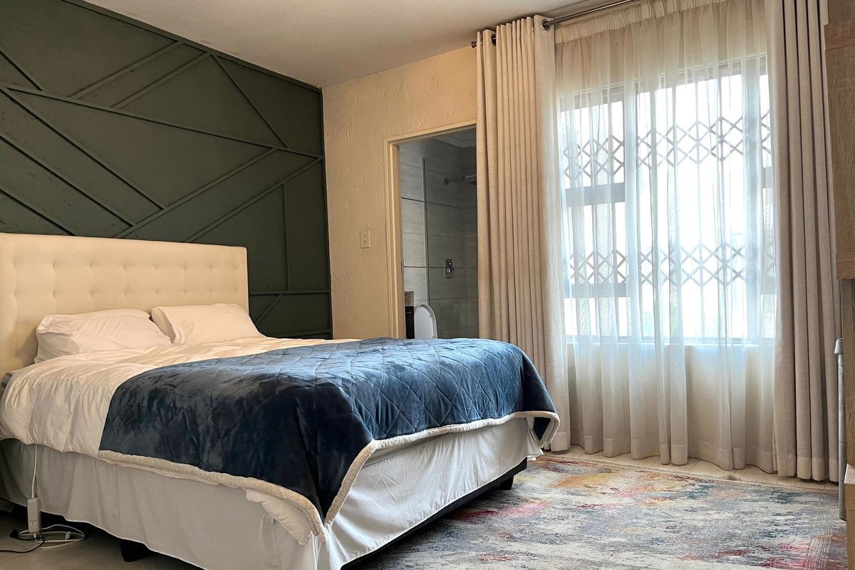A well-maintained bedroom featuring decorative wall paneling, tiled flooring, and an en-suite bathroom access, with natural light provided by a large window.