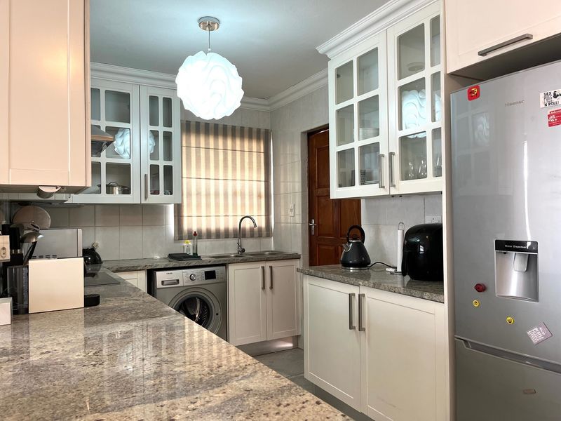 A functional kitchen featuring granite countertops, white cabinetry with glass-front uppers, tiled backsplash, and an integrated washing machine.