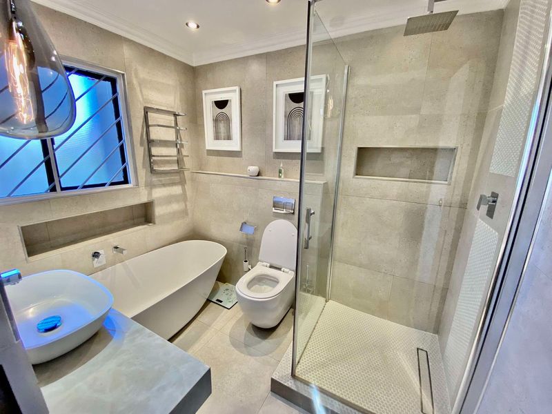 Modern bathroom featuring a freestanding bathtub, walk-in shower with rain head, wall-mounted toilet, and a stylish vessel sink with neutral stone-look tiling.