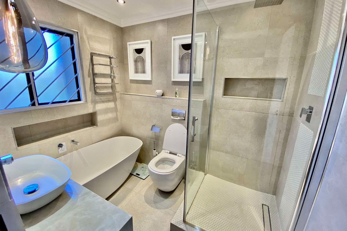 Modern bathroom featuring a freestanding bathtub, walk-in shower with rain head, wall-mounted toilet, and a stylish vessel sink with neutral stone-look tiling.