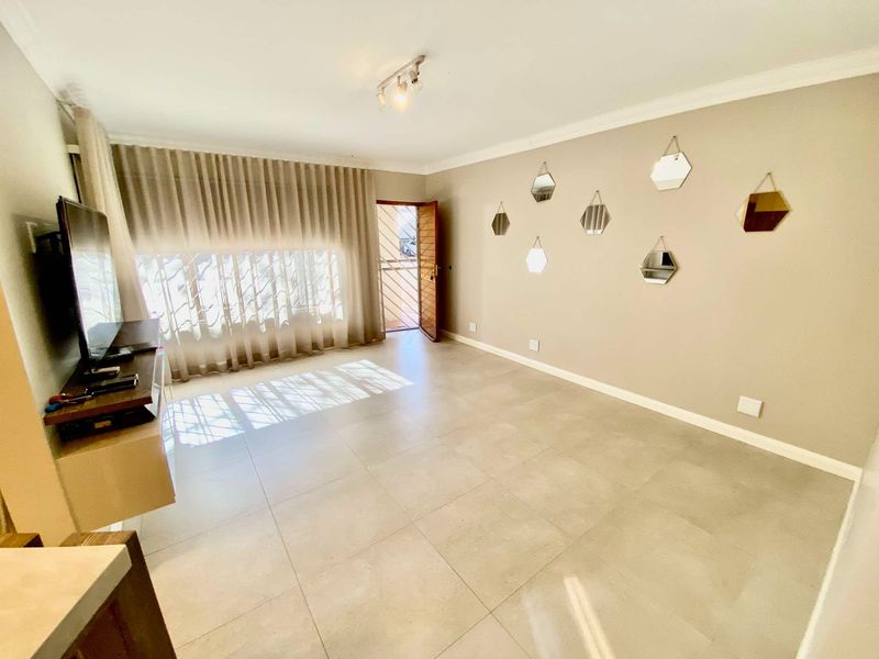 A bright living room featuring neutral tiled flooring, ceiling coving, and a security gate leading to the exterior.