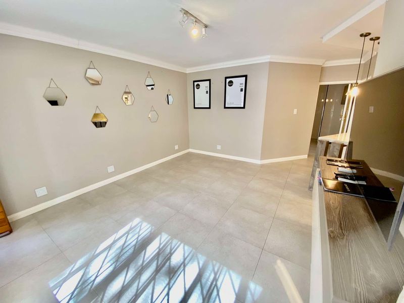 A bright, open-plan living area featuring neutral tiled flooring, modern track lighting, and decorative cornice detailing, providing a clean and versatile space.