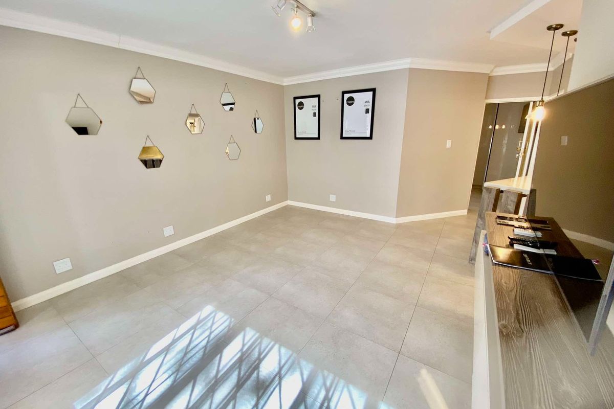 A bright, open-plan living area featuring neutral tiled flooring, modern track lighting, and decorative cornice detailing, providing a clean and versatile space.