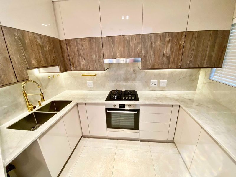 Modern kitchen featuring high-gloss cabinetry, stone countertops, integrated gas hob, built-in oven, and premium gold-tone fixtures with under-cabinet lighting.