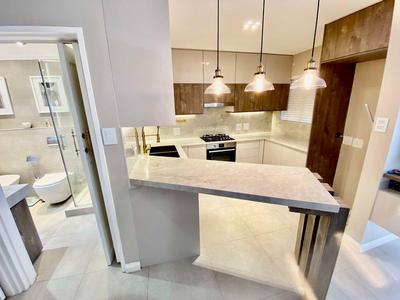 Modern kitchen featuring sleek cabinetry, stone countertops, a breakfast bar, and integrated appliances, with an adjacent bathroom visible through the doorway.