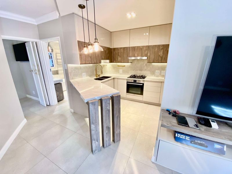 Modern open-plan kitchen featuring sleek cabinetry, stone countertops, a breakfast bar, and integrated appliances, seamlessly flowing into the living area.