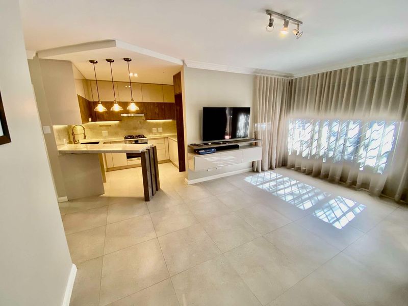 Modern open-plan living area featuring a sleek kitchen with stone countertops, gas hob, and integrated cabinetry, flowing into a bright, tiled lounge space.