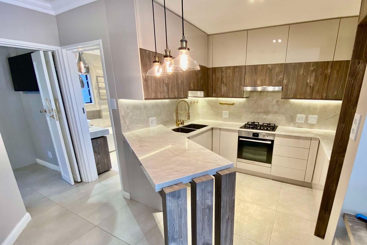 Modern kitchen featuring sleek two-tone cabinetry, stone countertops, integrated gas hob, built-in oven, and a stylish breakfast bar with feature pendant lighting.