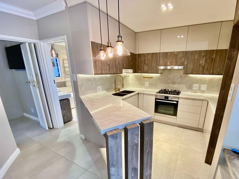Modern kitchen featuring sleek two-tone cabinetry, stone countertops, integrated gas hob, built-in oven, and a stylish breakfast bar with feature pendant lighting.