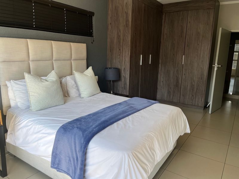 A well-maintained bedroom featuring dark wood built-in cupboards, neutral tiled flooring, and modern dark grey accent wall.