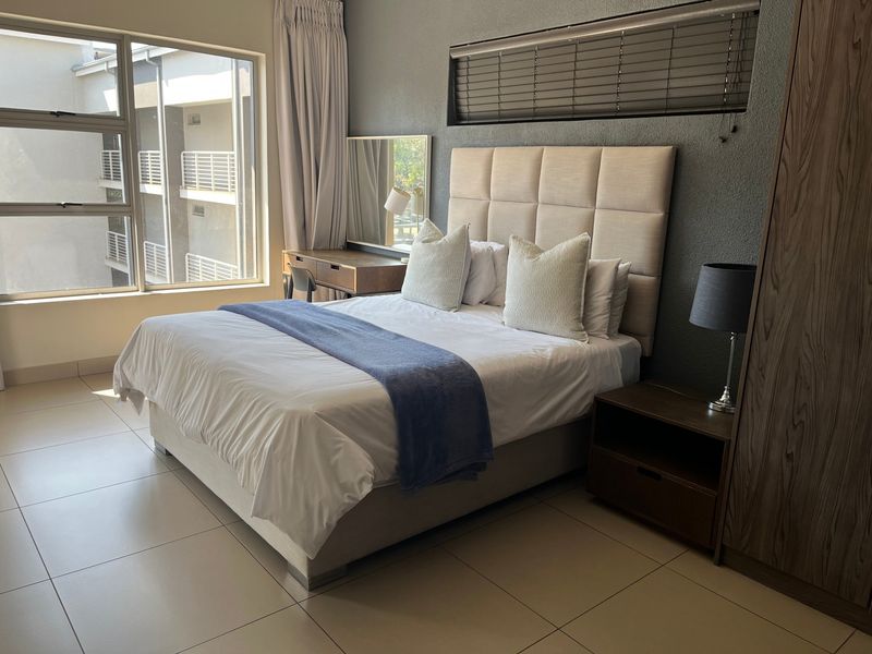 A well-maintained bedroom featuring tiled flooring, built-in wardrobe storage, and large windows with venetian blinds, offering a clean and functional living space.