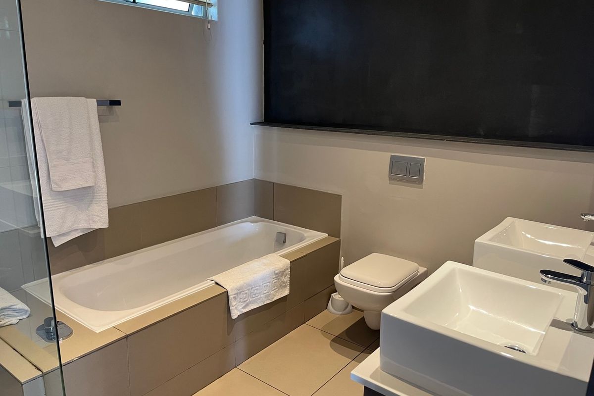 Modern bathroom featuring a built-in bathtub, wall-mounted toilet, and dual vessel sinks with contemporary chrome fixtures and neutral tiling.