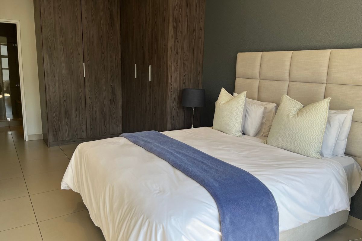 A well-maintained bedroom featuring dark wood built-in cupboards, neutral tiled flooring, and a modern dark accent wall.