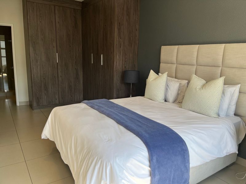 A well-maintained bedroom featuring dark wood built-in cupboards, neutral tiled flooring, and a modern dark accent wall.
