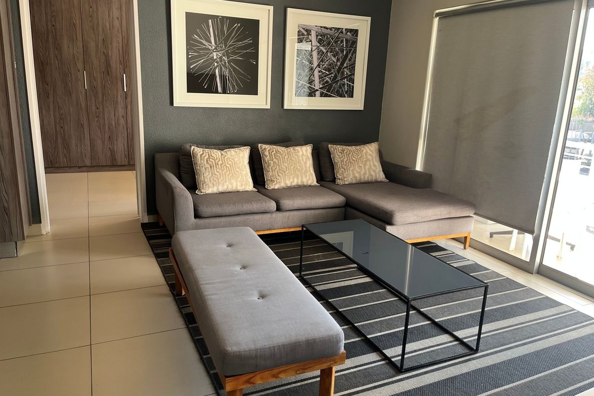 A modern living room featuring tiled flooring, a dark accent wall, and a large sliding glass door with a roller blind leading to the exterior.