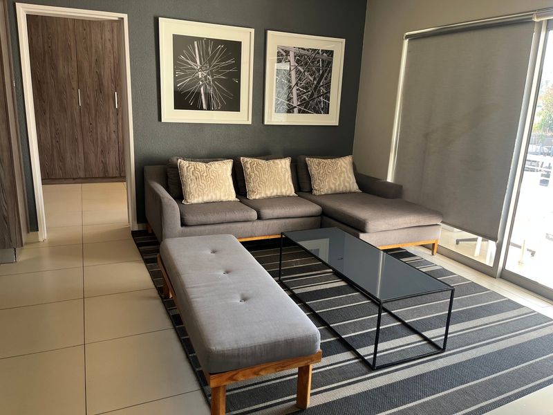 A modern living room featuring tiled flooring, a dark accent wall, and a large sliding glass door with a roller blind leading to the exterior.