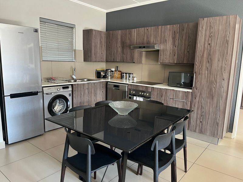Modern open-plan kitchen featuring wood-grain cabinetry, integrated appliances, tiled flooring, and a functional layout, seamlessly connecting to the dining area.