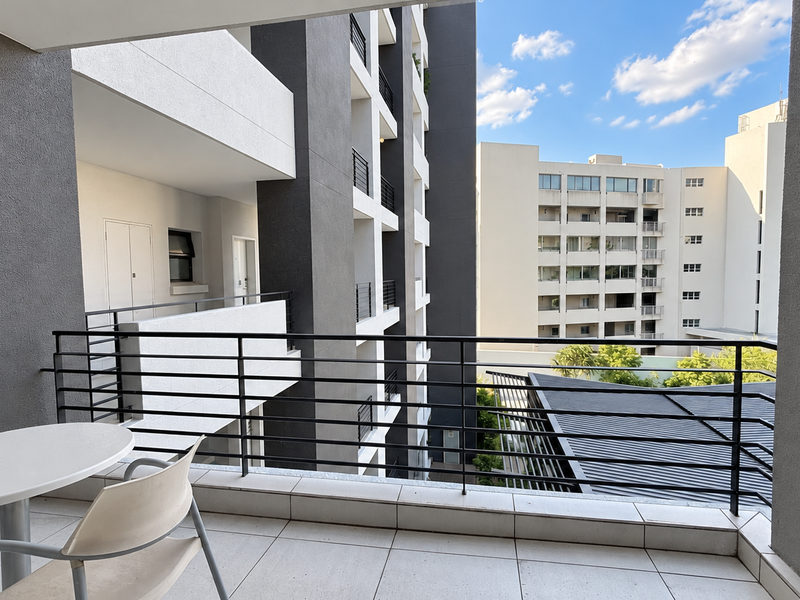 A modern apartment balcony featuring tiled flooring and a sleek metal balustrade, offering an open view of the surrounding residential complex.