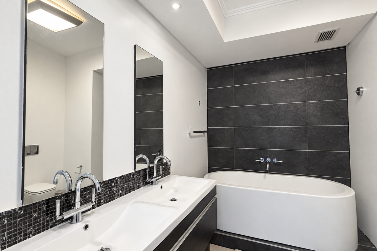 Modern bathroom featuring a double vanity with wall-mounted faucets, a sleek freestanding bathtub, and a striking dark tiled feature wall.