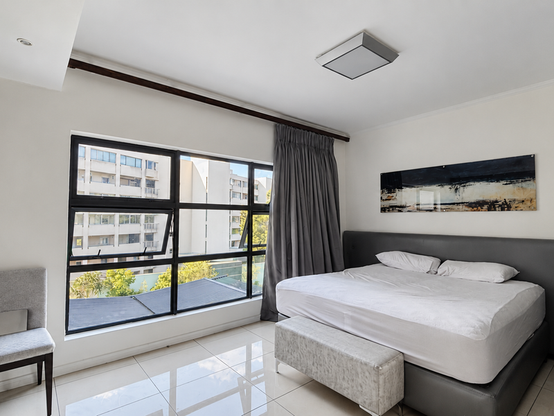 A bright bedroom featuring large aluminium-framed windows, tiled flooring, and a built-in wardrobe, offering a clean and modern living space.