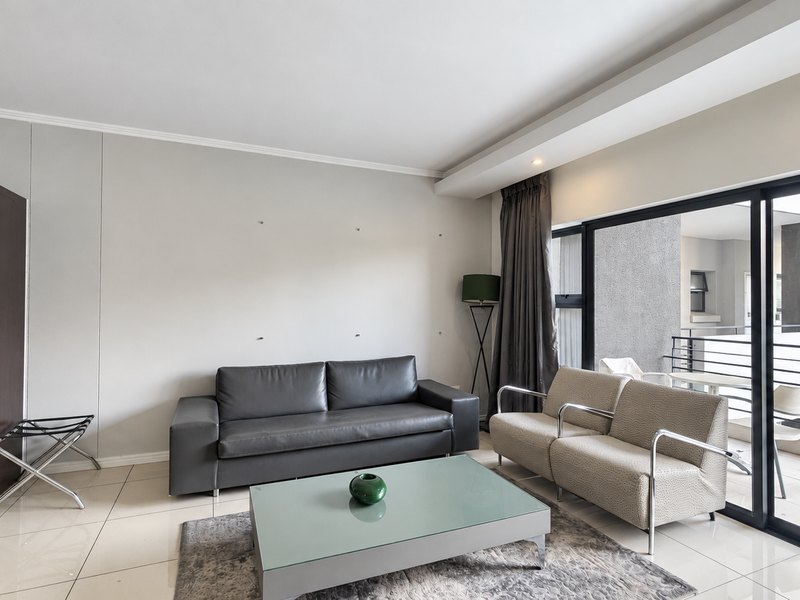 A bright living room featuring tiled flooring, recessed ceiling lighting, and large sliding glass doors that provide access to an attached balcony.