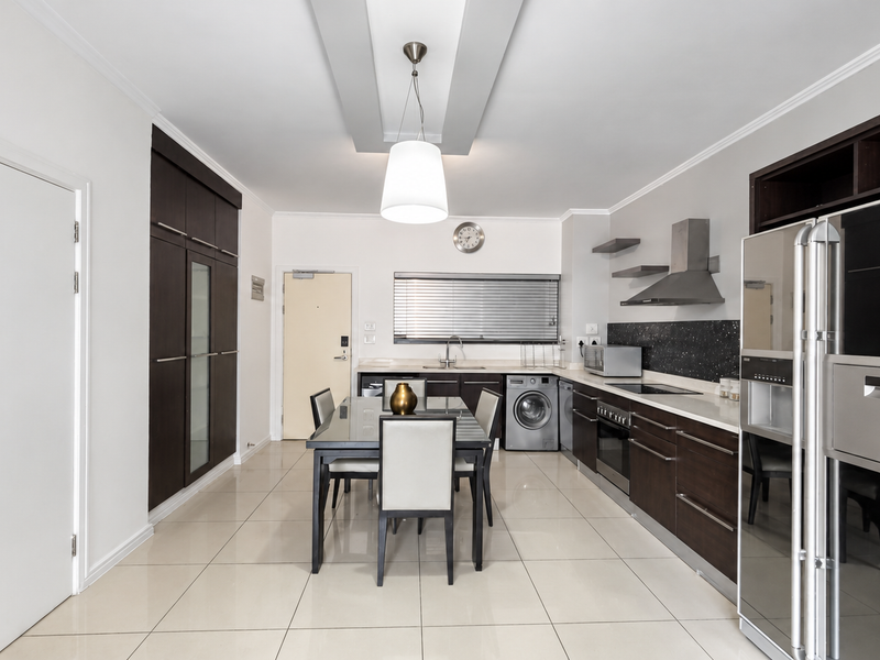 Modern open-plan kitchen and dining area featuring dark wood cabinetry, sleek countertops, integrated appliances, and polished tile flooring under a recessed ceiling.