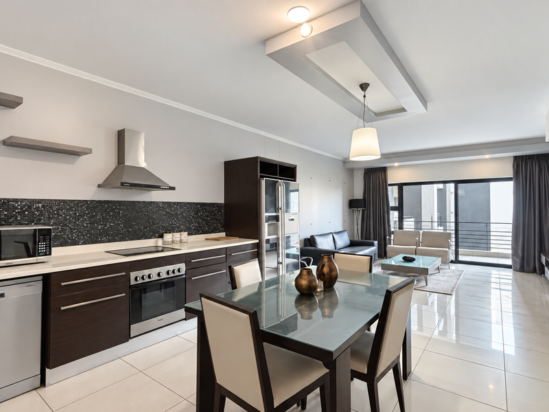 Modern open-plan kitchen and living area featuring dark wood cabinetry, mosaic backsplash, stainless steel appliances, and large sliding doors leading to a balcony.