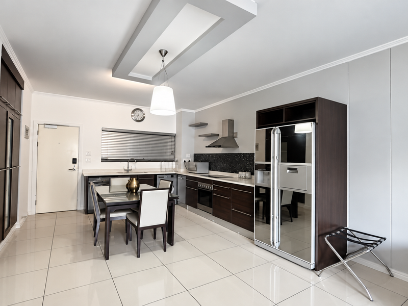 Modern open-plan kitchen featuring dark wood cabinetry, stainless steel appliances, tiled flooring, and a stylish recessed ceiling detail with pendant lighting.