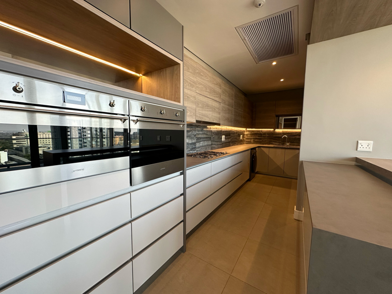 Modern, high-end kitchen featuring sleek cabinetry, built-in double ovens, gas hob, stone backsplash, and integrated lighting in a contemporary penthouse setting.
