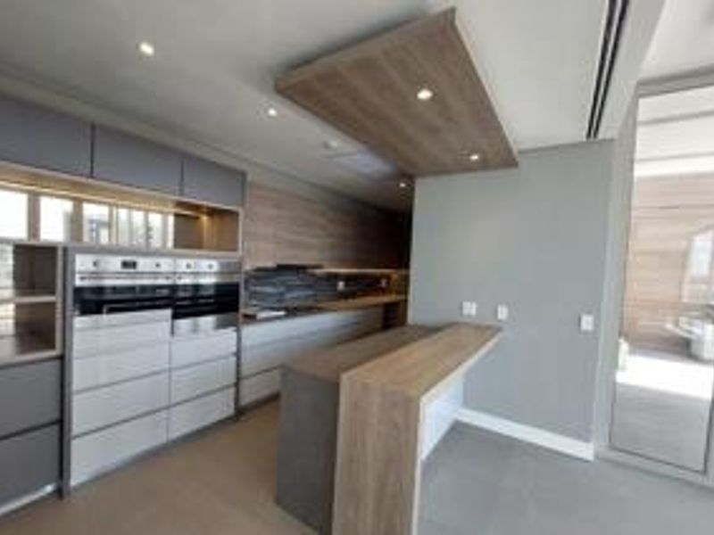 Modern kitchen featuring high-end built-in appliances, sleek cabinetry, stone countertops, and a breakfast bar, with direct access to an outdoor balcony area.