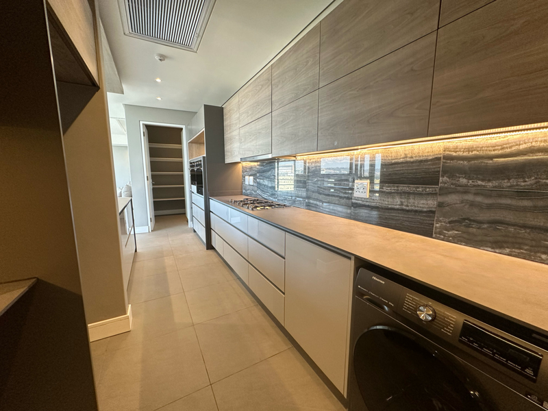 Modern kitchen featuring sleek wood-grain cabinetry, stone countertops, integrated appliances, and high-end finishes with ambient under-cabinet lighting.