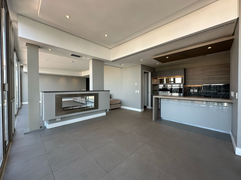 Spacious open-plan living and kitchen area featuring a modern built-in fireplace, high-end integrated appliances, sleek cabinetry, and large windows with neutral tiled flooring.