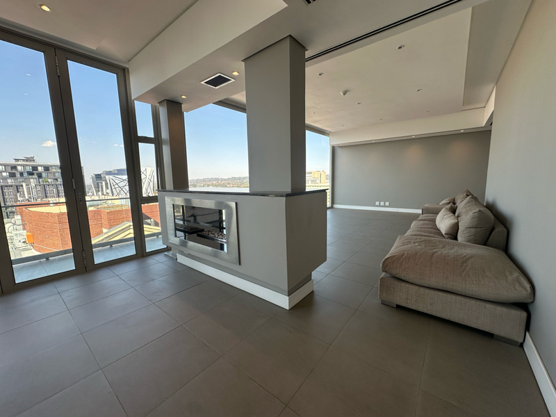 Spacious open-plan living area featuring a modern built-in fireplace, large format floor tiles, and expansive floor-to-ceiling windows with panoramic city views.