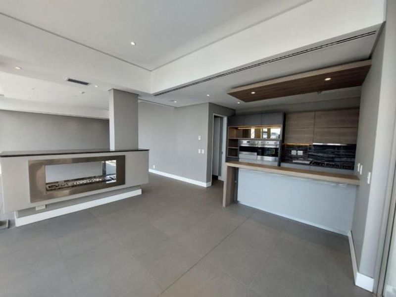 Modern open-plan living area featuring a sleek kitchen with integrated appliances, a breakfast bar, and a contemporary built-in fireplace.