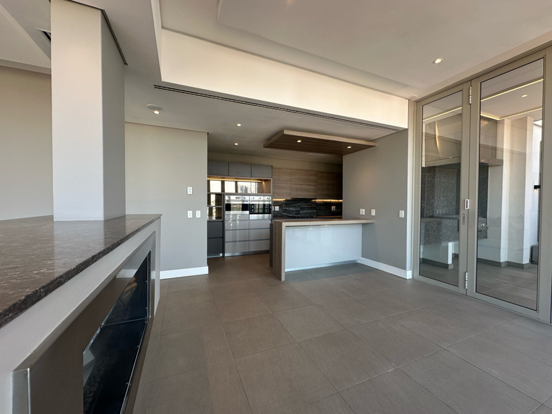 Spacious open-plan living area featuring a modern kitchen with integrated appliances, a built-in fireplace, and large glass doors leading to an outdoor space.