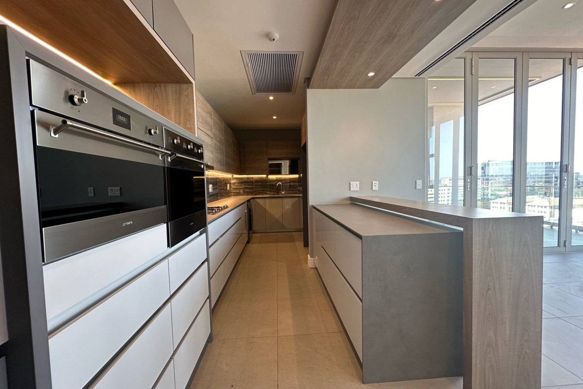 Modern, high-end kitchen featuring sleek cabinetry, built-in ovens, a stone island, and seamless access to an outdoor balcony area.