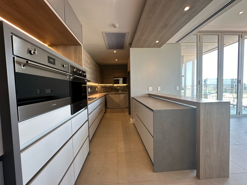 Modern, high-end kitchen featuring sleek cabinetry, built-in ovens, a stone island, and seamless access to an outdoor balcony area.