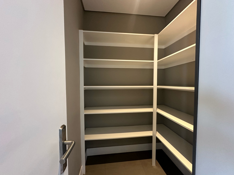 A clean, modern walk-in pantry or scullery area featuring extensive built-in white shelving and neutral wall finishes.