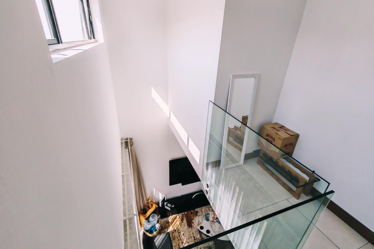 A high-ceiling living area viewed from above, featuring a modern glass balustrade, tiled floors, and natural light from clerestory windows.