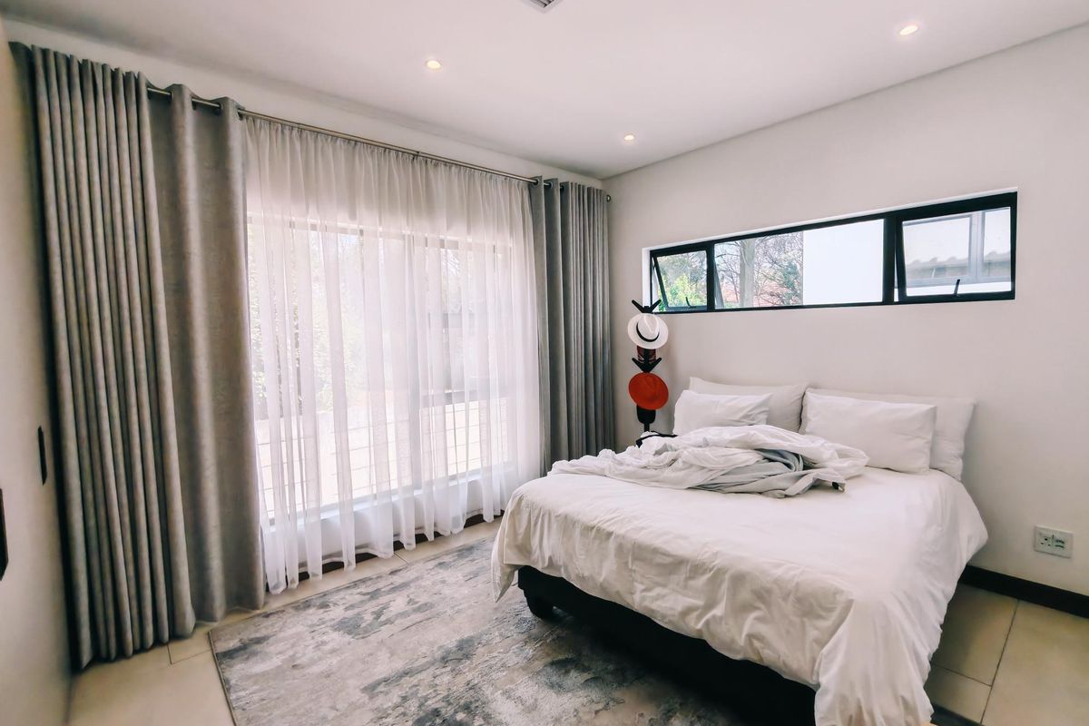 A bright and modern bedroom featuring tiled flooring, recessed downlights, ducted air conditioning, and large windows with floor-to-ceiling curtains.