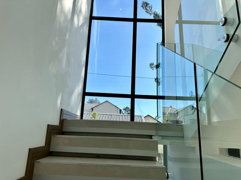 A bright, modern staircase featuring a glass balustrade and a large floor-to-ceiling window that allows for abundant natural light.