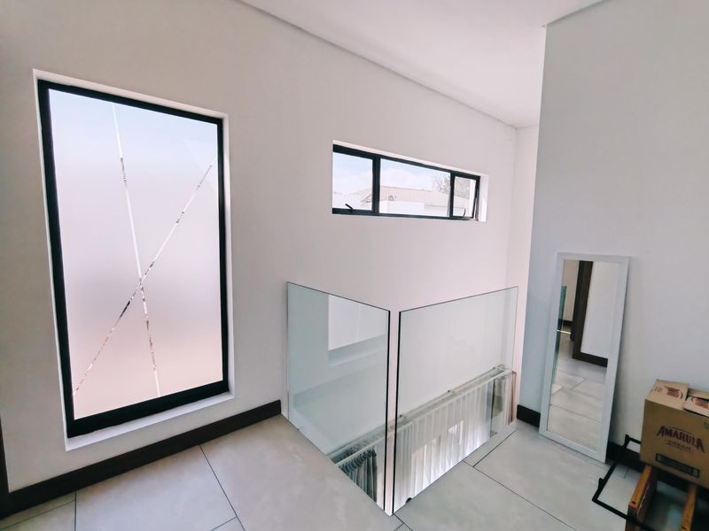A bright, modern landing area featuring sleek glass balustrades, large frosted windows, and neutral tiled flooring, creating an open and airy transition space.
