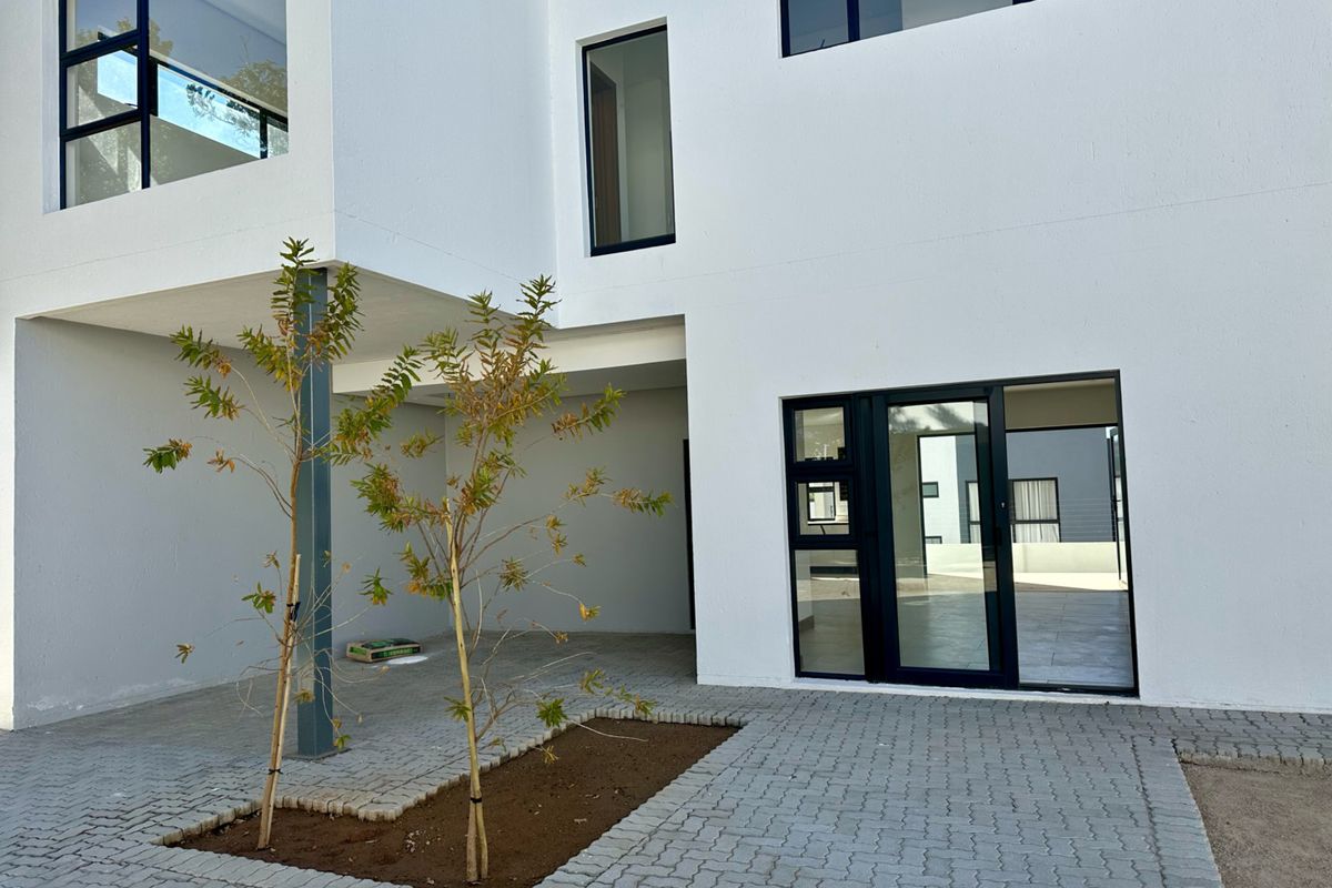 Modern townhouse rear elevation featuring clean white facade, paved courtyard area, and large aluminium-framed windows and sliding doors.