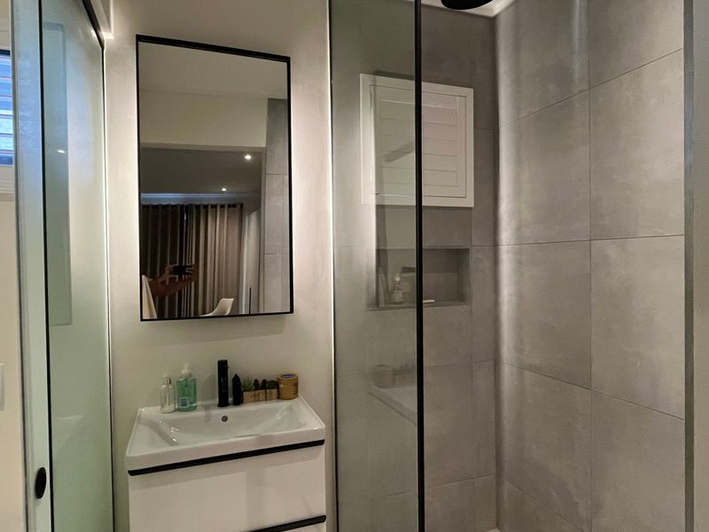 Modern bathroom featuring a sleek vanity, walk-in shower with glass screen, built-in shower niche, and contemporary grey wall tiling.