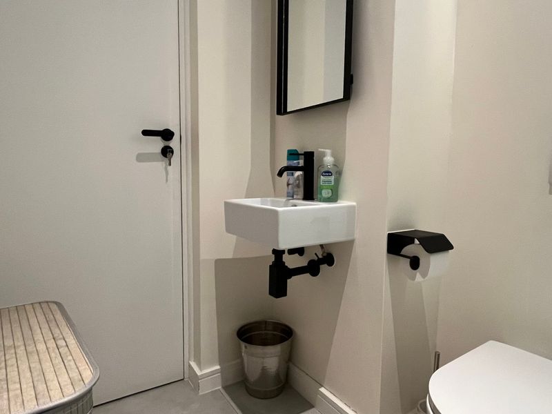 A compact modern bathroom featuring a wall-mounted basin with black fixtures, a wall-hung toilet with a flush plate, and a minimalist design.