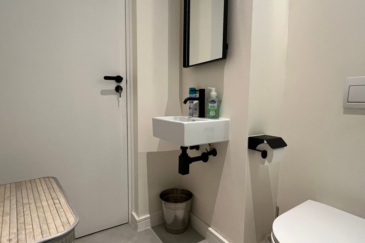 A compact modern bathroom featuring a wall-mounted basin with black fixtures, a wall-hung toilet with a flush plate, and a minimalist design.